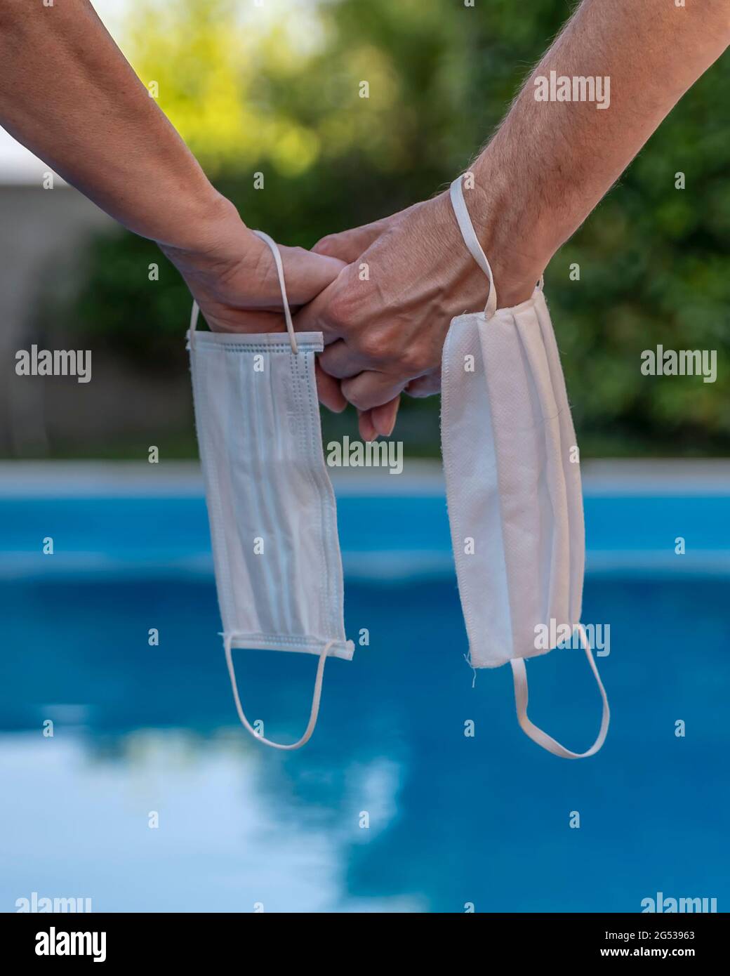 Une main femelle et une main mâle se soutiennent mutuellement, ayant un masque protecteur sur le poignet, sur un fond de bleu waté Banque D'Images