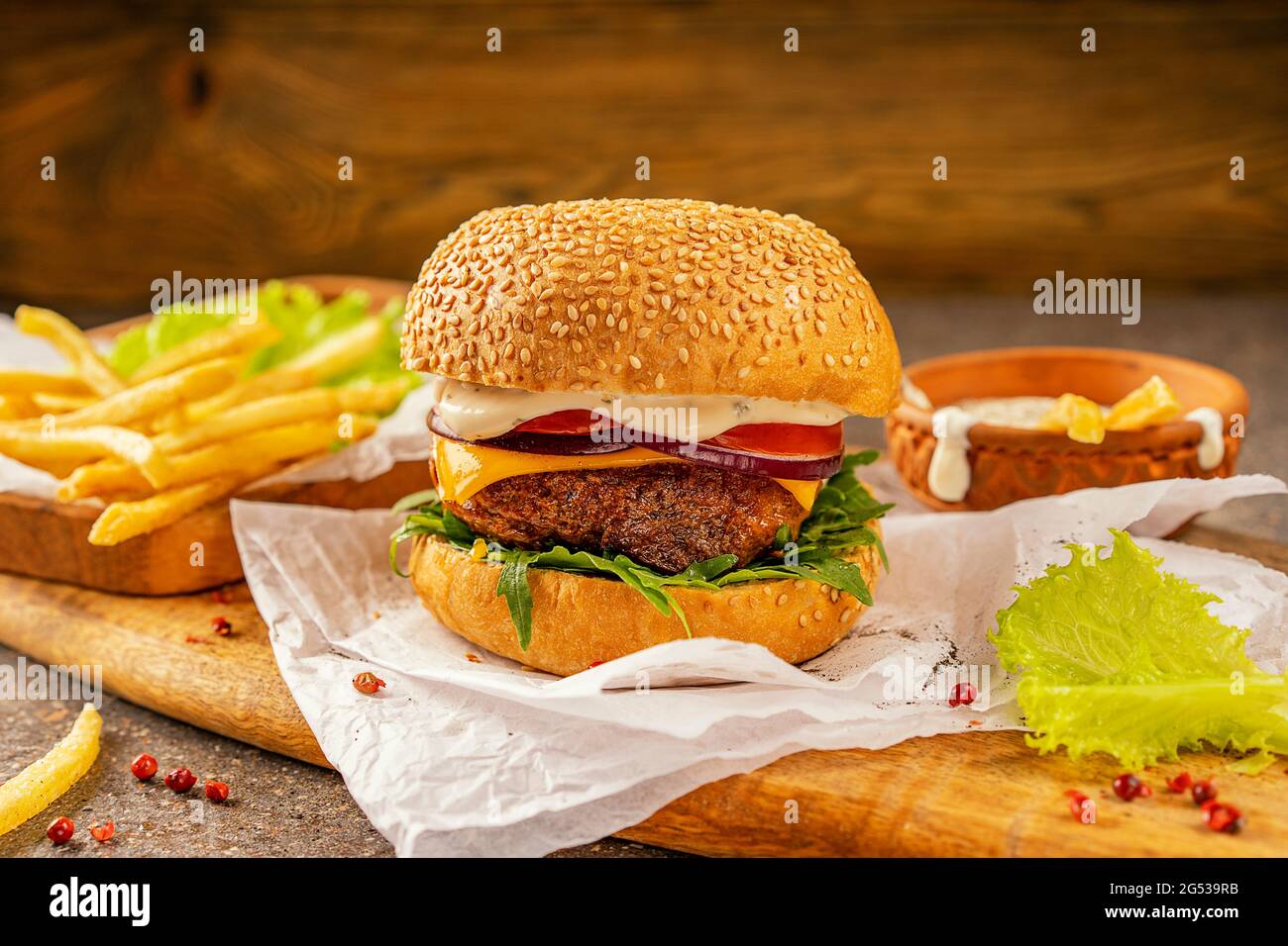 Délicieux hamburger et frites chaudes prêts à consommer. Une planche à découper en bois de mangue dans un style rustique. Salade d'herbes fraîches et d'arugula. Profitez de votre Banque D'Images