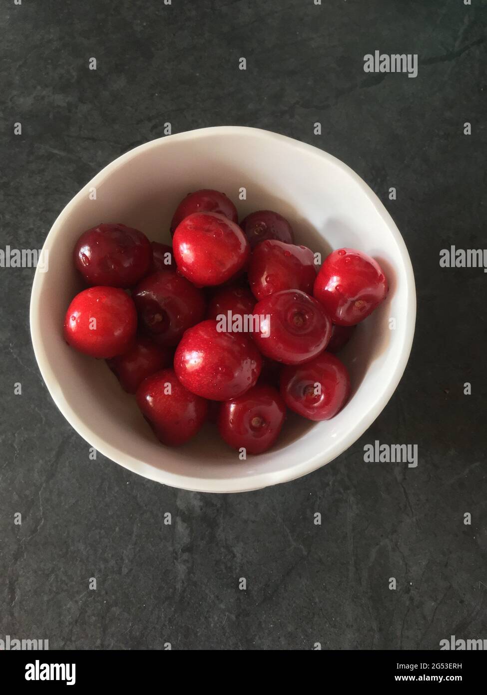 Cerises mûres rouges et bordeaux dans une plaque blanche sur fond noir de table Banque D'Images