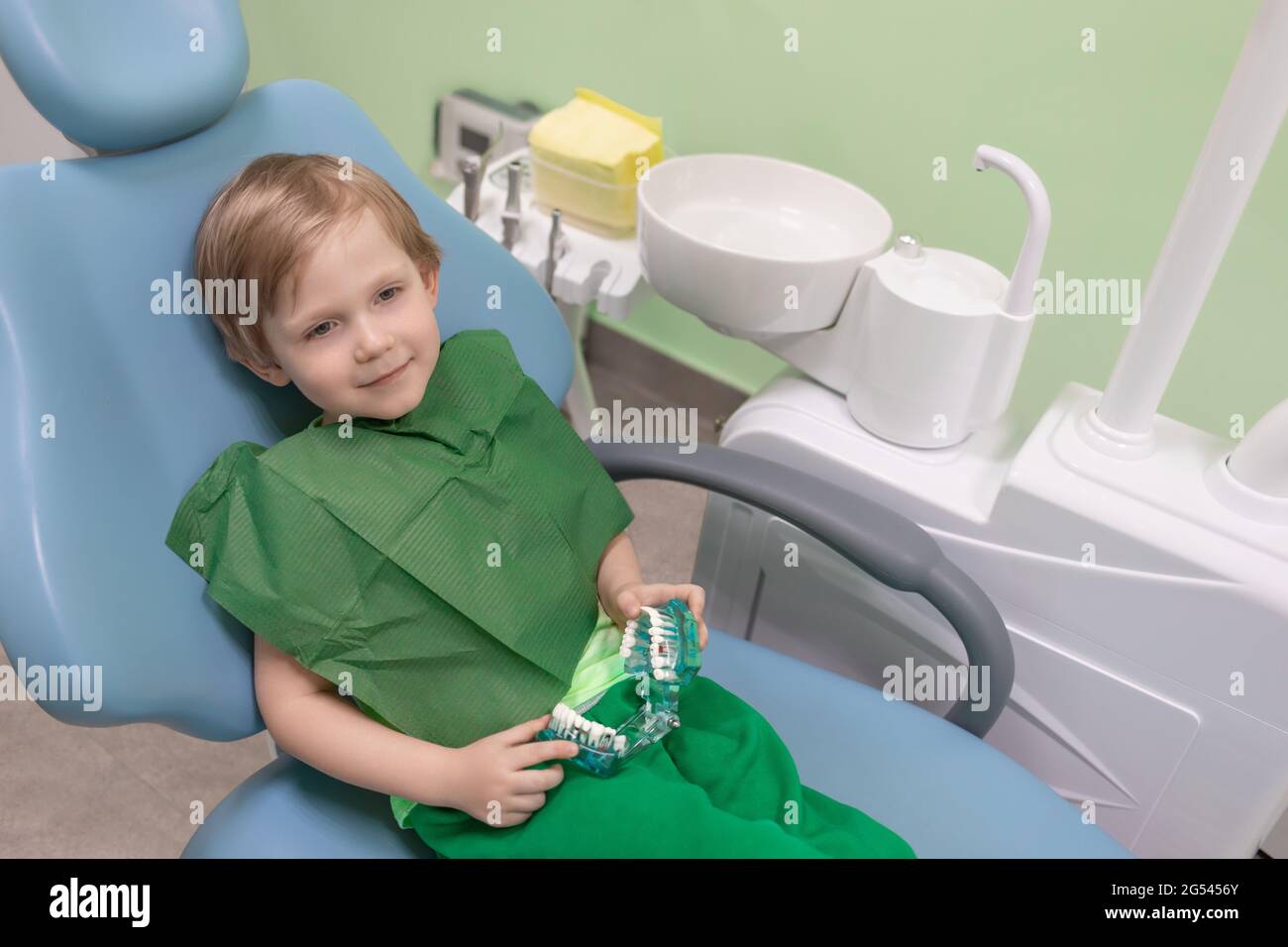 Décontracté enfant content homme assis dans la chaise chez le dentiste dans  les mains de la mâchoire avec des dents blanches jouet et des accessoires.  Concept de traitement indolore et anesthésie i