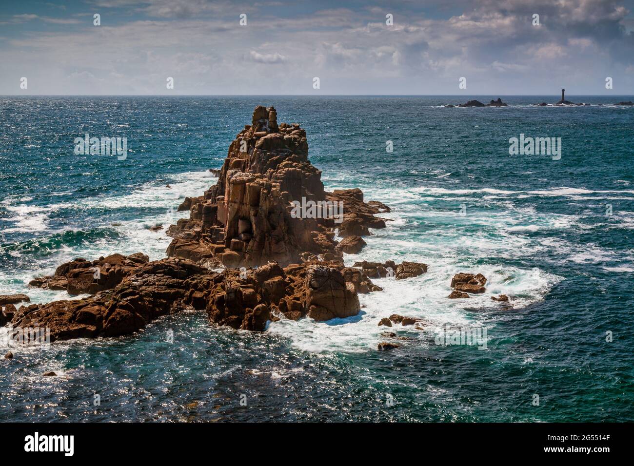 La mer tourbillonne autour de la formation rocheuse du Chevalier armé, à la fin du Land à Cornwall, avec le phare des Longships au loin. Banque D'Images