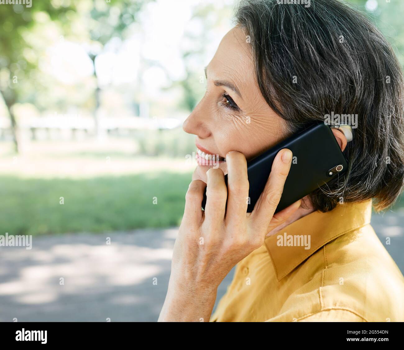 Une femme mature avec une prothèse auditive a une vie entière et peut entendre son interlocuteur au téléphone. Solution auditive et technologie innovante Banque D'Images