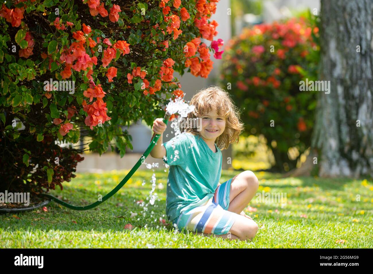 Les enfants jouent avec le tuyau d'arrosage dans la cour. Jeux d'été pour enfants  en plein air. Petit garçon jouant avec le tuyau d'eau dans l'arrière-cour.  Jeu de fête pour les enfants
