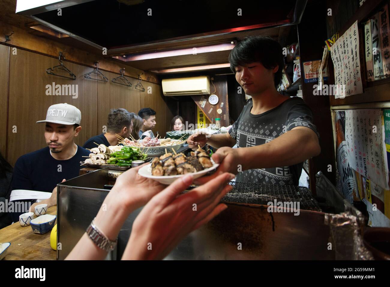 Réception d'une assiette de brochettes yakitori dans un petit restaurant à Omoide Yokocho, Tokyo, Japon Banque D'Images