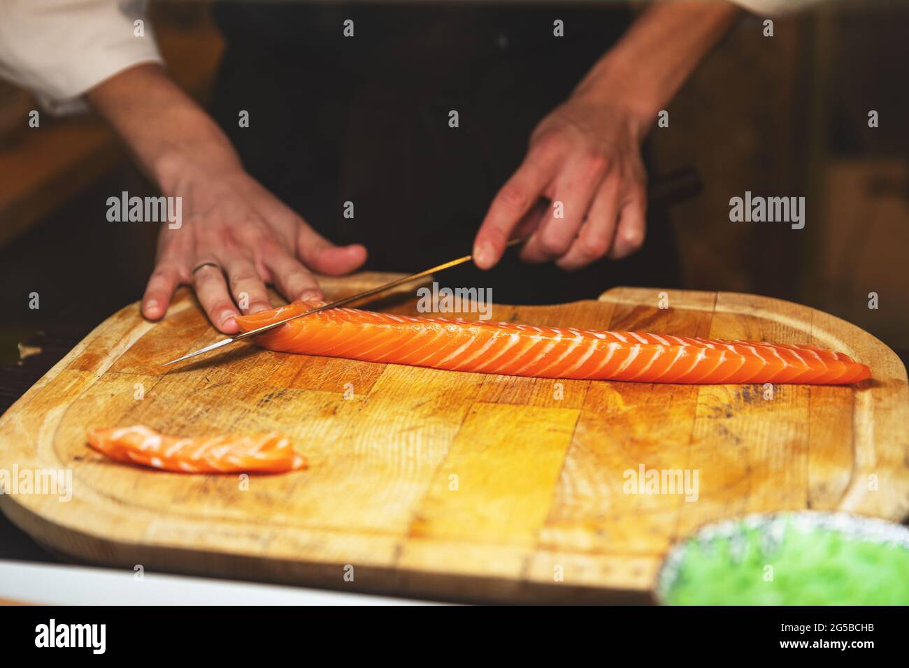 Le chef coupe le filet de saumon sur la planche à découper en bois Banque D'Images