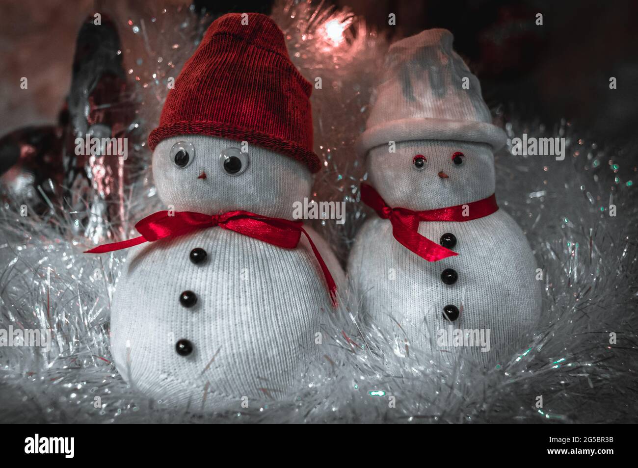 Bonhommes de neige mignons en casquettes recouverts de guirlande à Noël. Banque D'Images