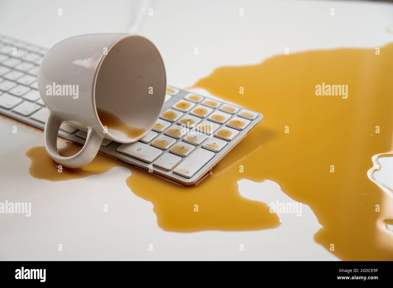 Tasse de café noir renversée sur le clavier de l'ordinateur sur la table blanche. Banque D'Images Tasse de café noir renversée sur le clavier de l'ordinateur sur la table blanche. Banque D'Images
