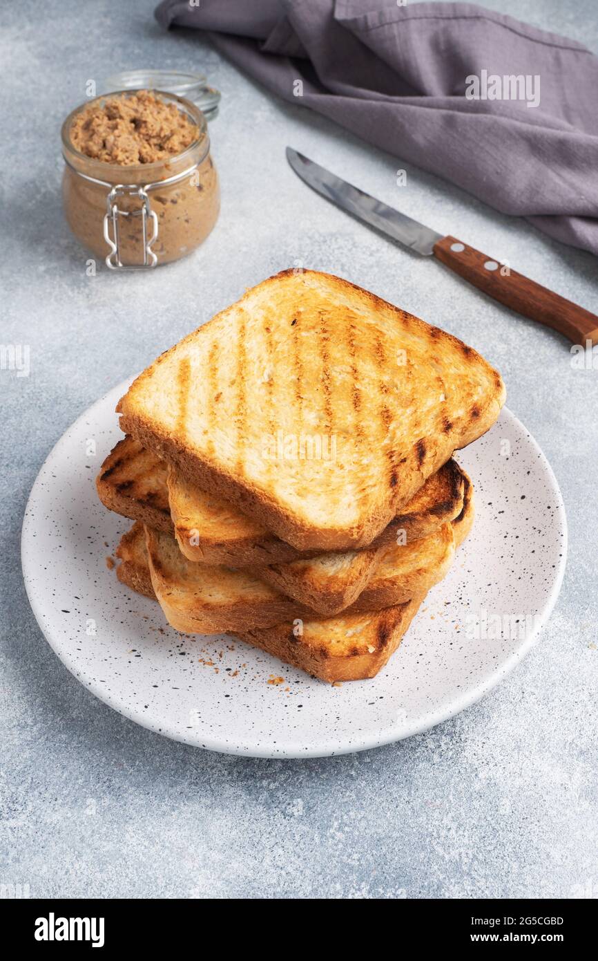 Pain grillé croustillant pour des sandwiches sur une assiette sur une table en béton gris UN pot de pâté de poulet. Banque D'Images Pain grillé croustillant pour des sandwiches sur une assiette sur une table en béton gris UN pot de pâté de poulet. Banque D'Images