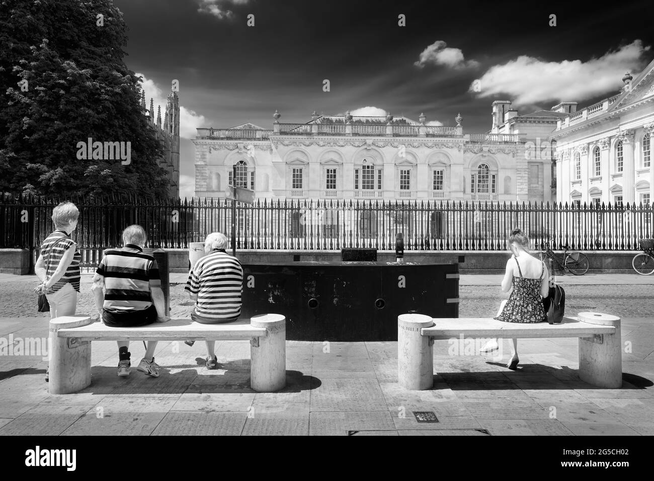 Trois touristes âgés et une étudiante sur les bancs en face du bâtiment Old Schools à l'université de Cambridge, Angleterre. Banque D'Images