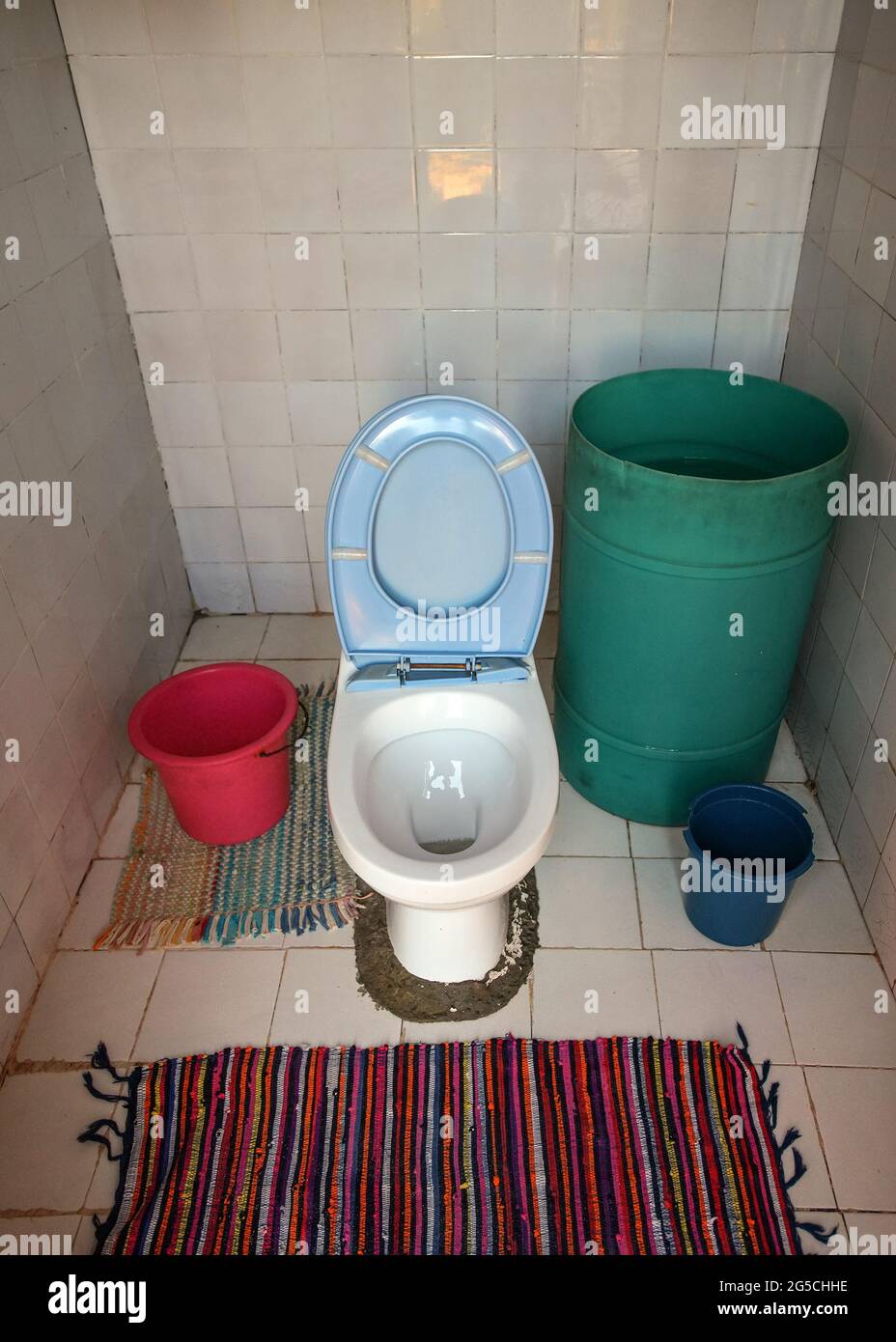 toilettes provisoires en porcelaine sans mécanisme de rinçage installé dans la pièce sans tuyaux ni plomberie, baril vert avec eau à proximité Banque D'Images