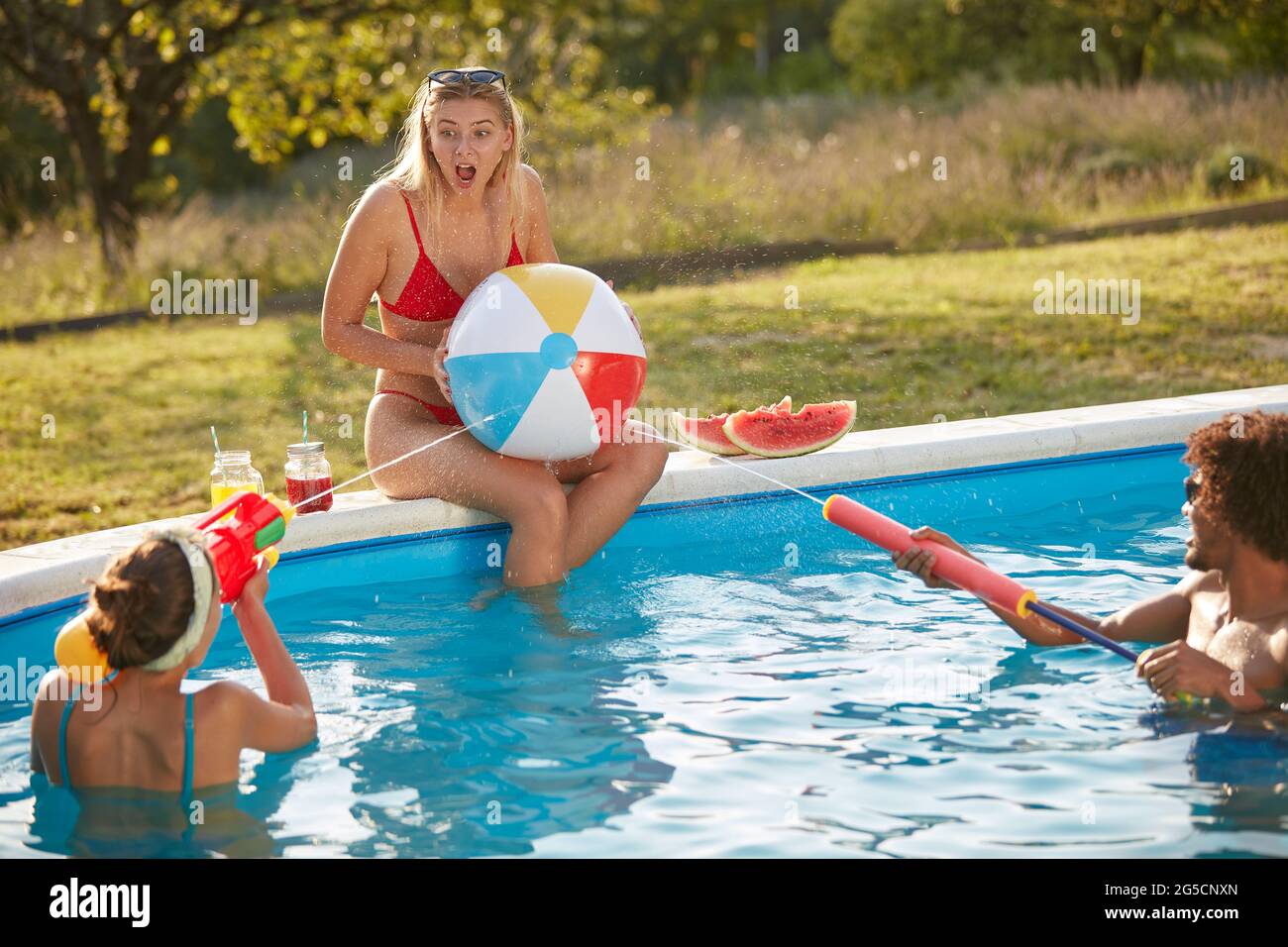 groupe de jeunes adultes s'amusant dans une piscine, jouant avec des pistolets à eau Banque D'Images