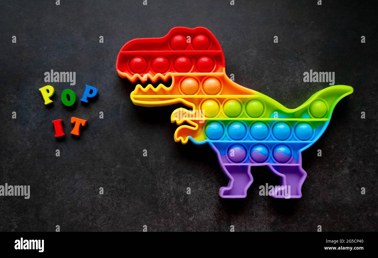 Jouet pop il dinosaure couleurs arc-en-ciel sur un fond noir avec des lettres multicolores et des lettres - Pop it. Banque D'Images