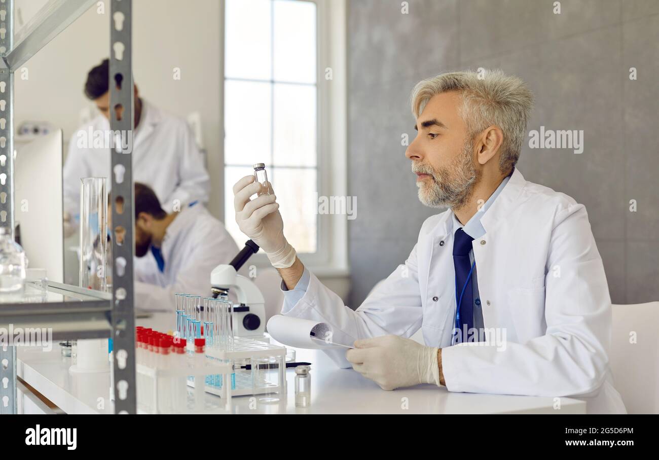 Scientifique sérieux en blouse de laboratoire et gants travaillant sur le nouveau vaccin en laboratoire médical Banque D'Images