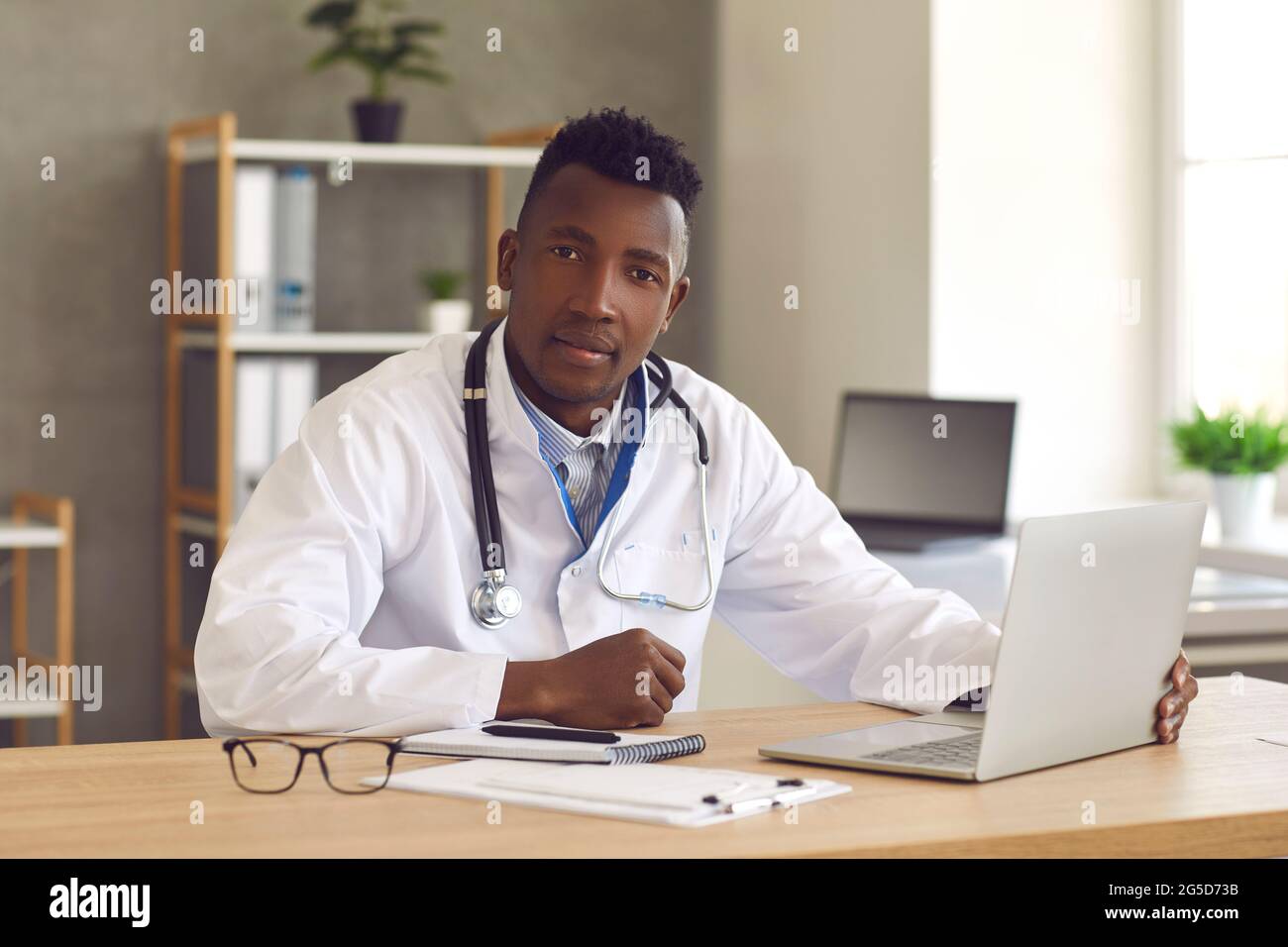 Joyeux médecin noir assis au bureau et utilisant un ordinateur portable pour un appel vidéo avec le patient Banque D'Images