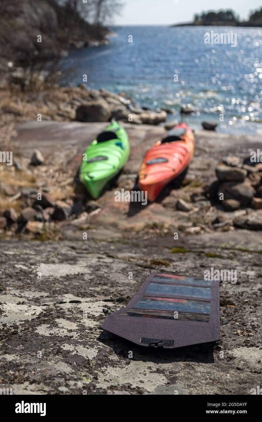 Les panneaux solaires portables se trouvent sur la rive pierreuse de l'accumulation d'énergie, sur le fond des kayaks garés et de la belle vue de mer. Banque D'Images