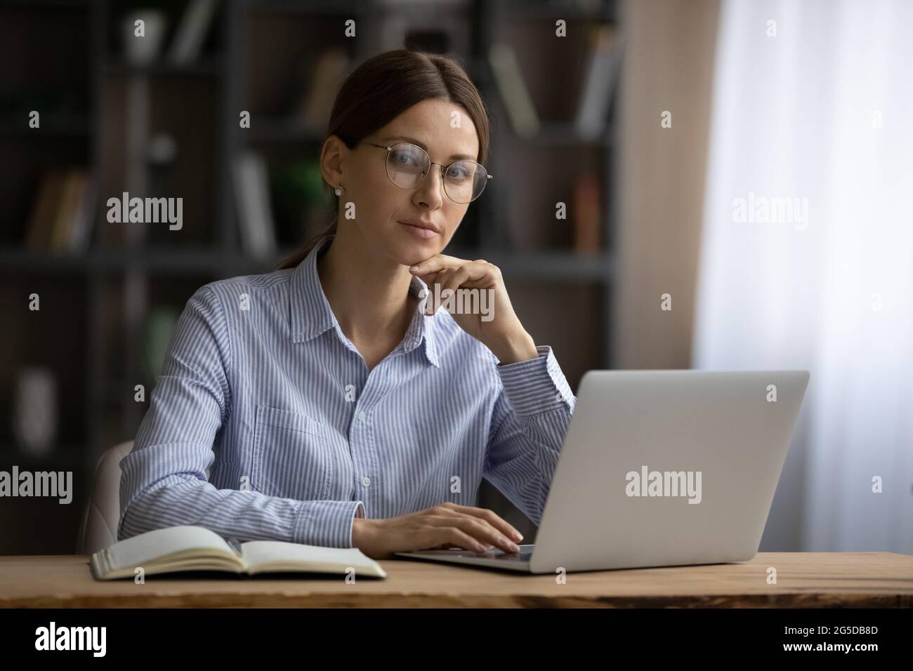 Portrait d'une femme d'affaires heureuse des années 30 en lunettes posant au bureau. Banque D'Images