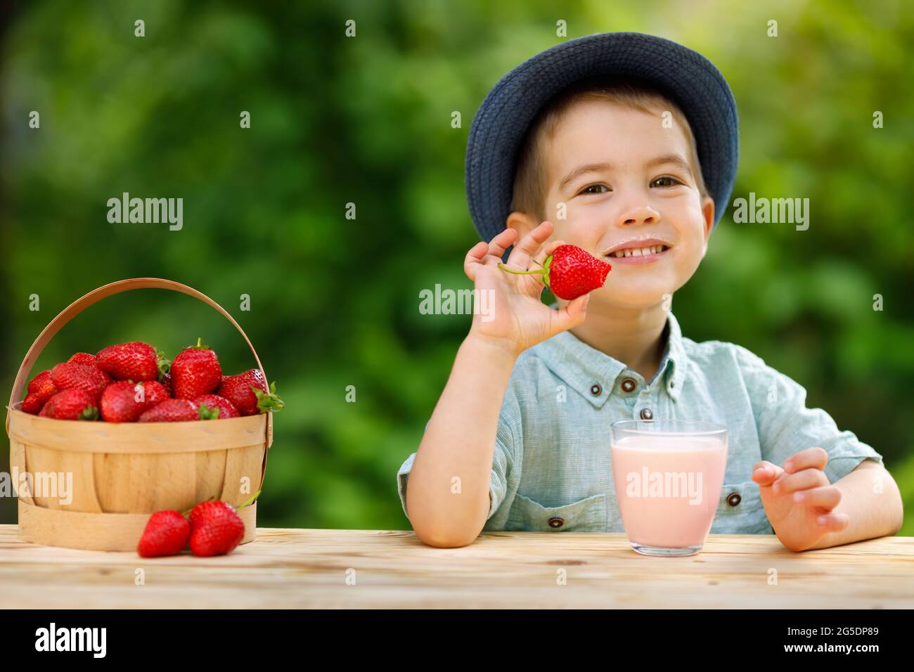 un petit garçon mange des fraises mûres et des boissons de yaourt à base de verre Banque D'Images