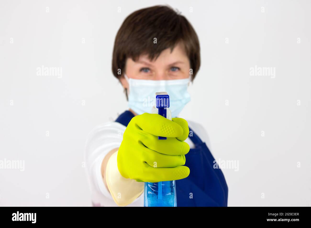 Dose courte d'une femme de nettoyage tenant un détergent avec un vaporisateur. Femme en uniforme et gants en caoutchouc tenant un spray nettoyant avec du liquide de nettoyage Banque D'Images