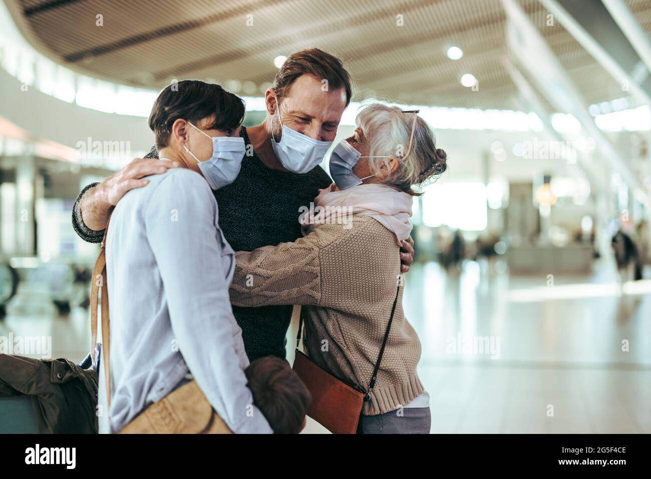 Femme âgée recevant sa famille à l'aéroport après l'arrivée du vol. Une femme âgée accueille son fils et sa famille à l'aéroport après une pandémie. Banque D'Images