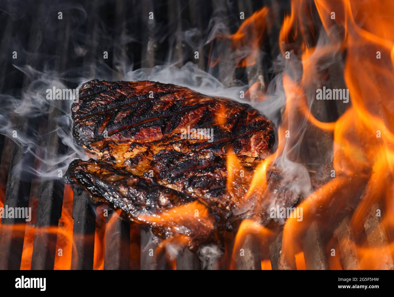 Gros plan sur des steaks de bœuf à la rivée et fumant sur une grille extérieure à feu ouvert avec grille en fonte métallique, vue en grand angle Banque D'Images