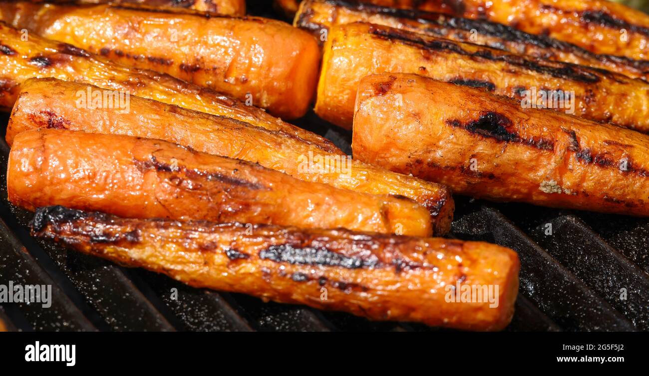 Gros plan sur la cuisson des carottes fraîches dans le gril extérieur au charbon de bois avec grille en fonte métallique, vue en grand angle Banque D'Images