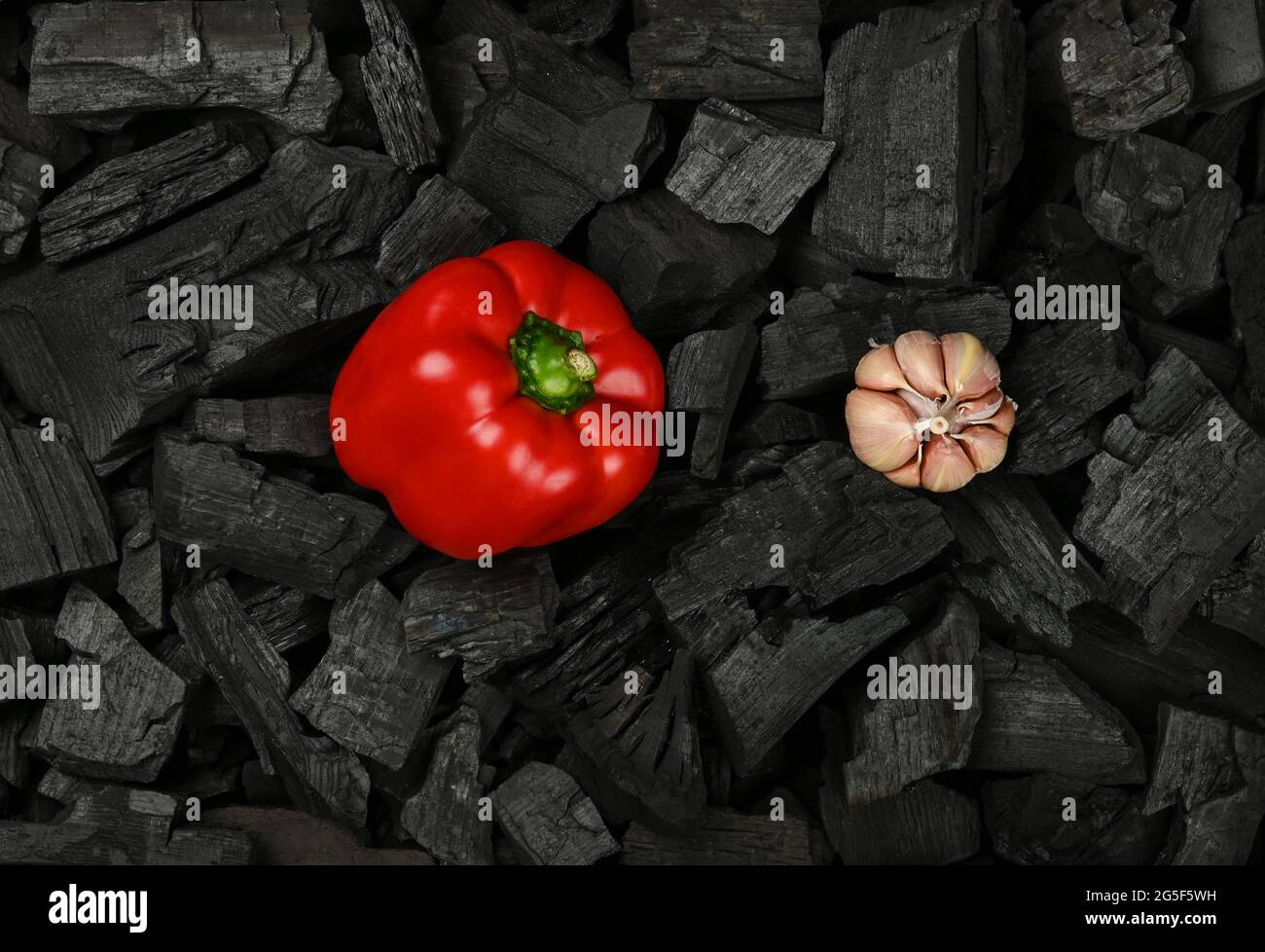 Gros plan sur le poivron rouge brut et l'ail sur des morceaux de charbon de bois en morceaux noirs prêts pour la cuisson au barbecue, vue du dessus en hauteur, directement au-dessus Banque D'Images