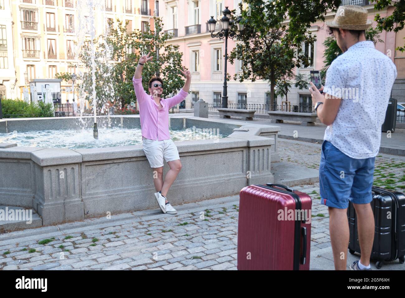 Homme prenant une photo de son ami heureux à la fontaine d'une place de la ville. Banque D'Images