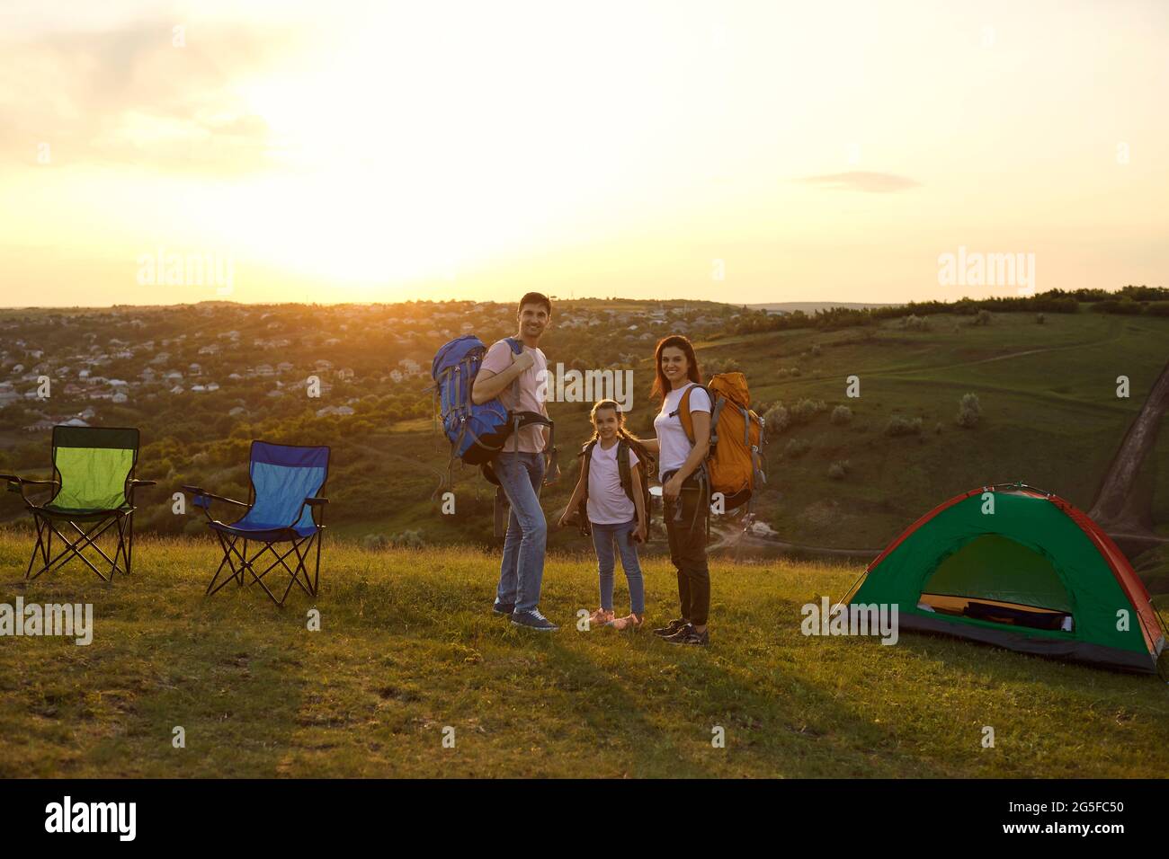 Bonne famille sur le camping d'été en montagne. Fille Adorble et parents debout sur le terrain de camping pendant le coucher du soleil Banque D'Images