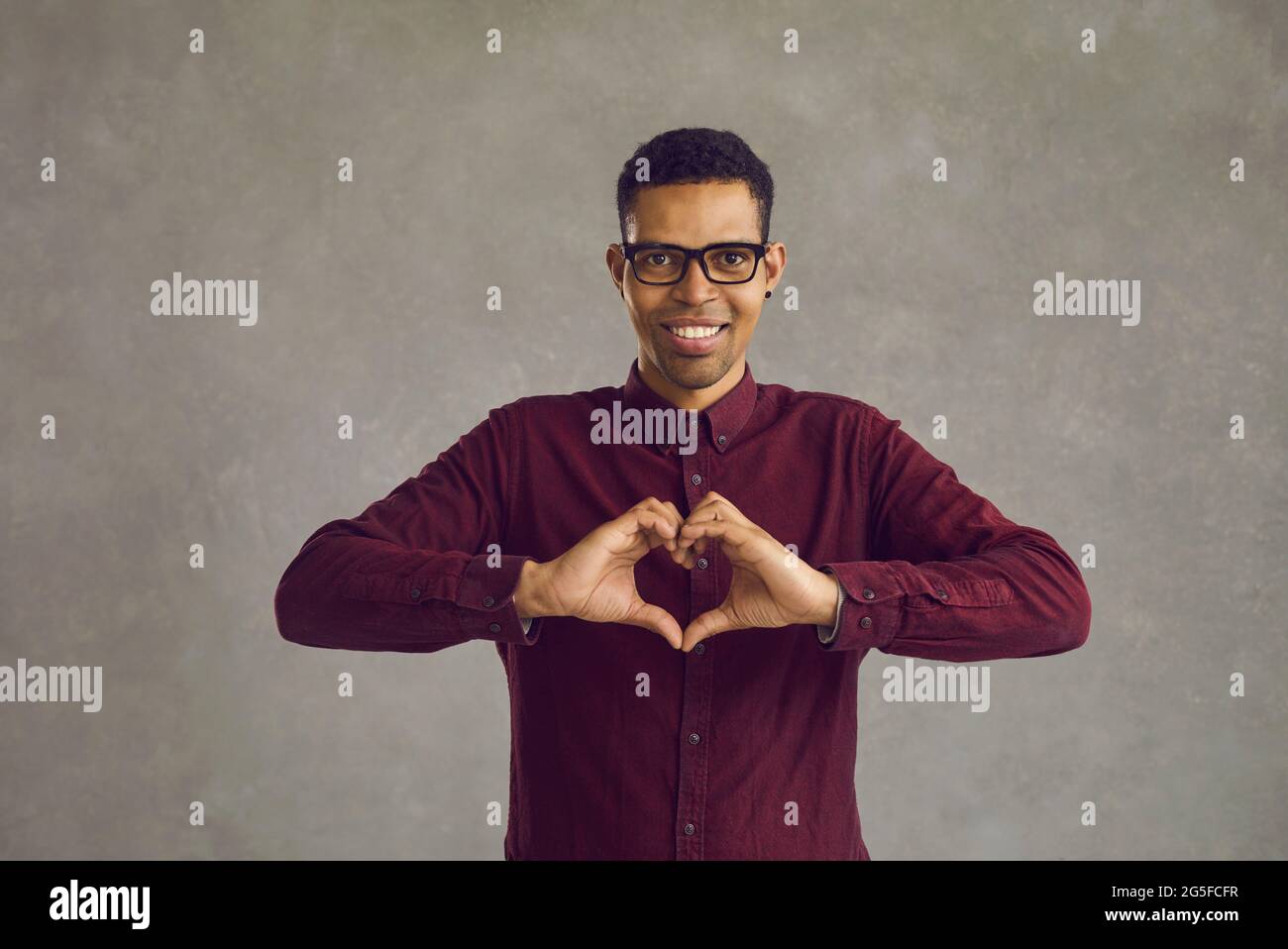 Portrait d'un jeune homme afro-américain faisant un geste de coeur tout en se tenant sur fond gris. Banque D'Images
