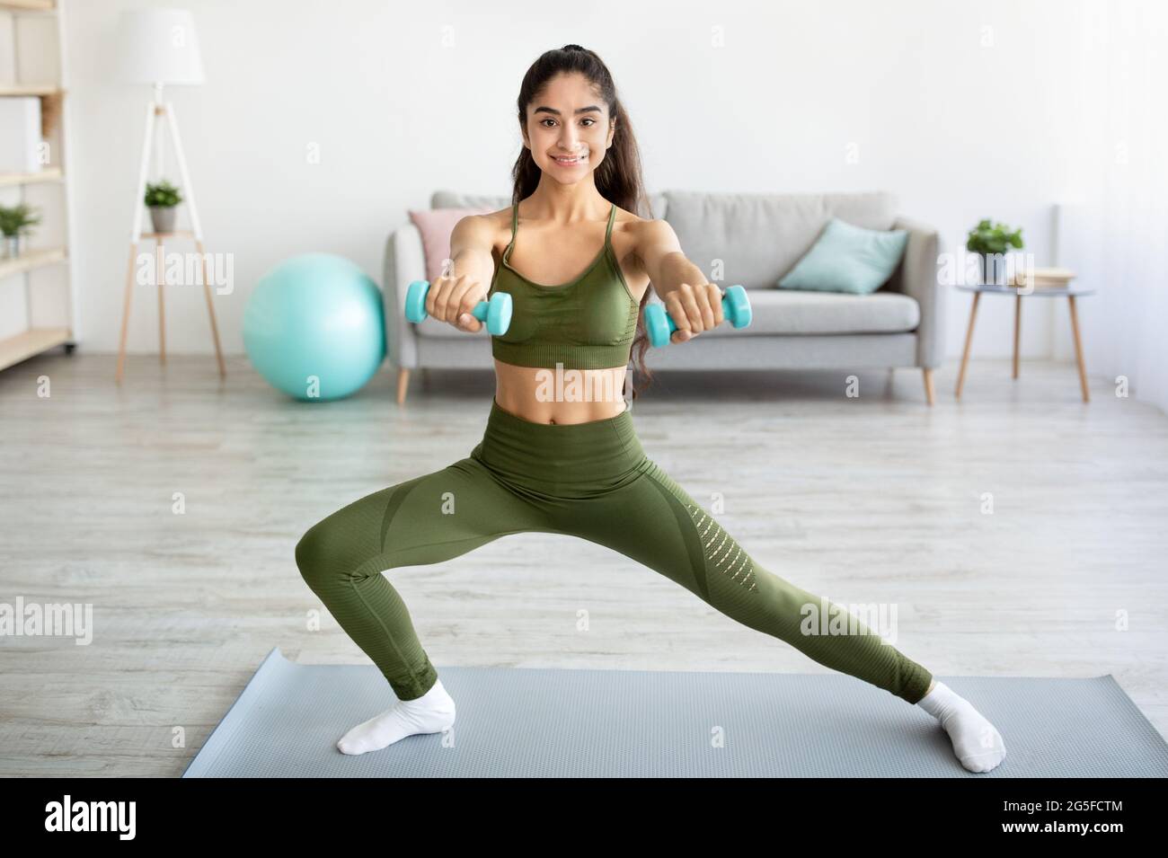Concept d'entraînement de force. Femme indienne athlétique faisant des exercices avec des haltères à l'intérieur, pleine longueur. Joyeuse dame de l'est travaillant les muscles du bras, l Banque D'Images