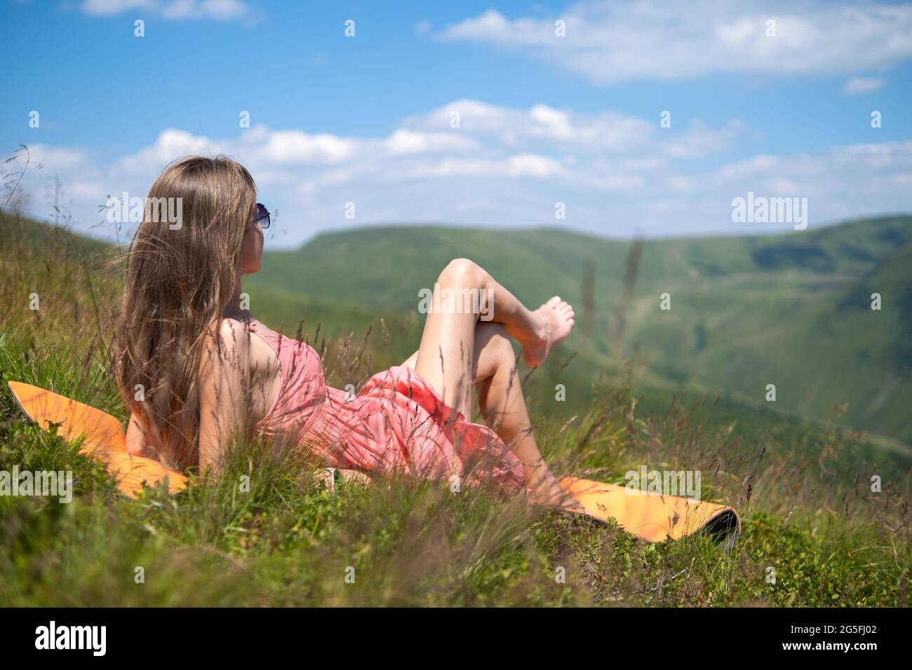 Jeune femme en robe rouge couché sur un pré vert herbacé lors d'une chaude journée ensoleillée dans les montagnes d'été profitant de la vue sur la nature. Banque D'Images