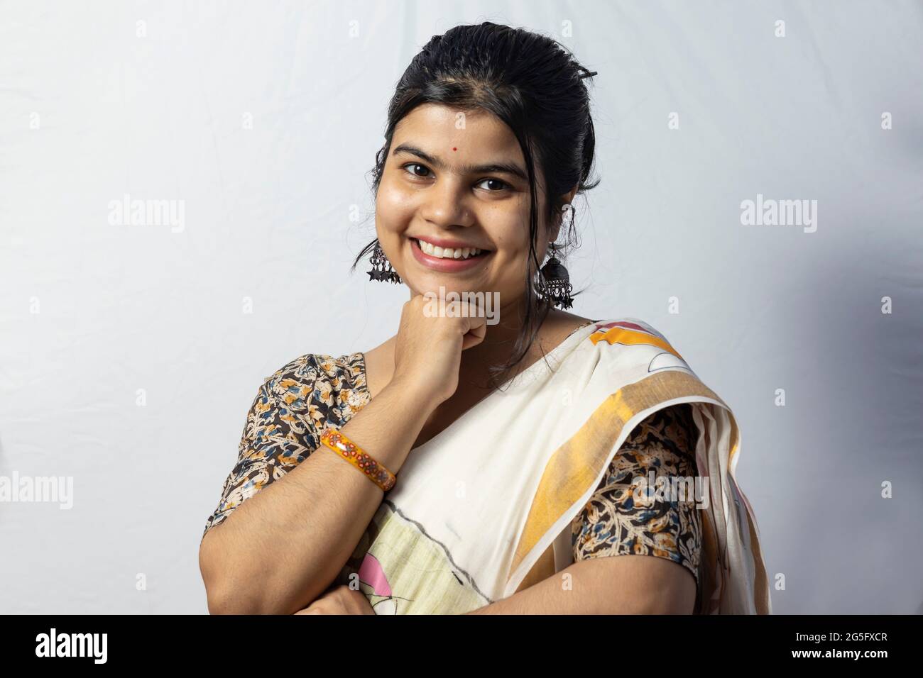 Isolée sur fond blanc une femelle indienne en saree sourit à l'appareil photo avec la main sous le menton pose sur fond blanc Banque D'Images
