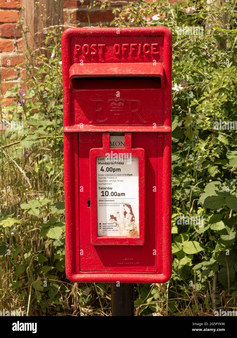 Boîte aux lettres de bureau de poste en fonte rouge montée sur un poteau devant une haie Banque D'Images