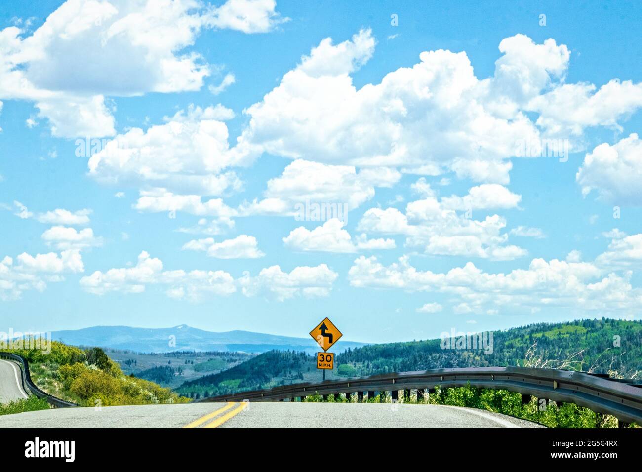 Route tortueuse dangereuse à travers les montagnes du Colorado montrant la falaise et la vallée très en dessous et panneau de route par rail de garde sous un beau ciel avec des nuages moelleux Banque D'Images