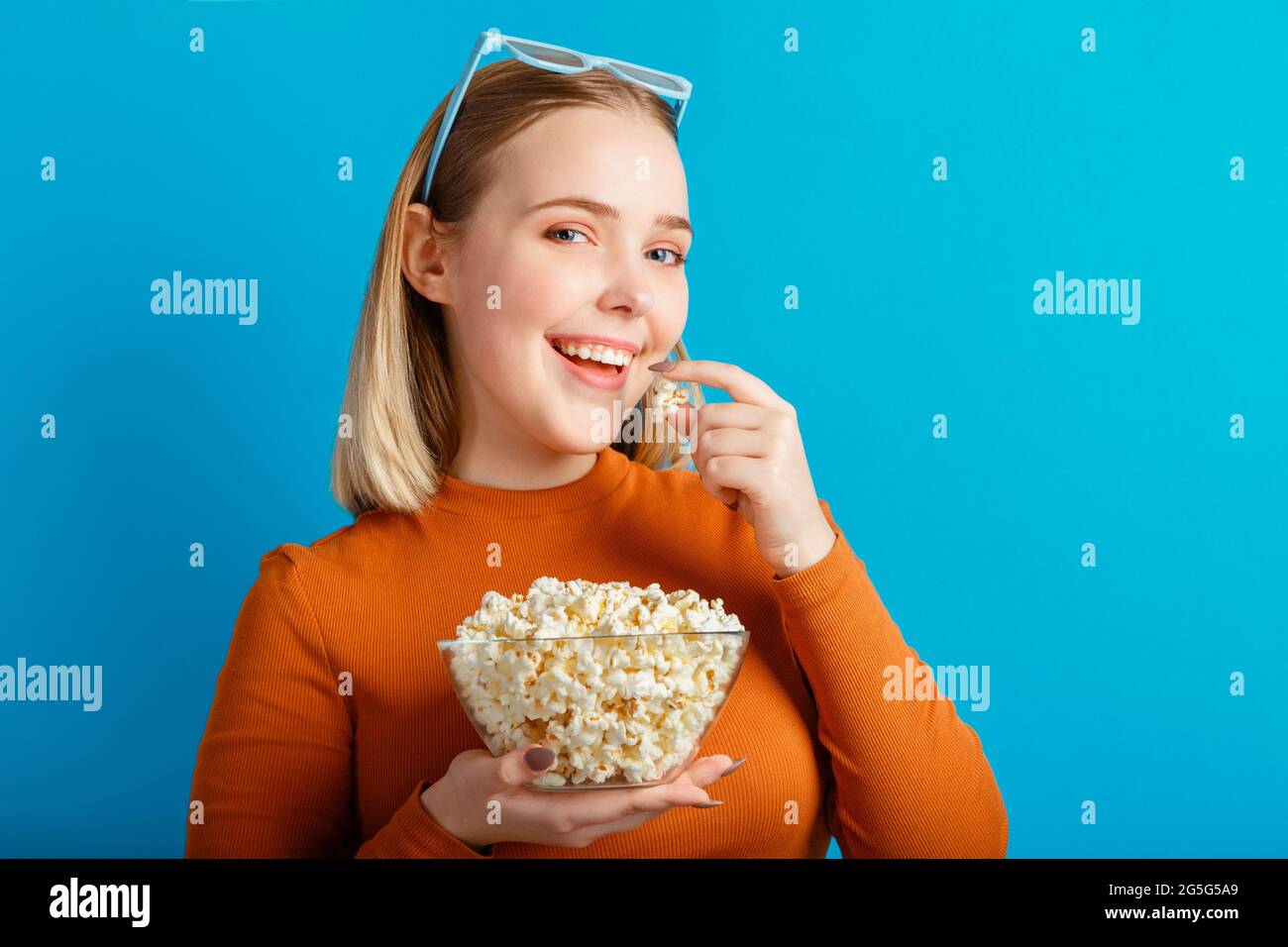 Jeune femme en lunettes de cinéma regardant un film en 3d. Une jeune fille qui souriait, regarde un film dans des verres, mange du pop-corn avec un espace de copie isolé sur une couleur bleue Banque D'Images