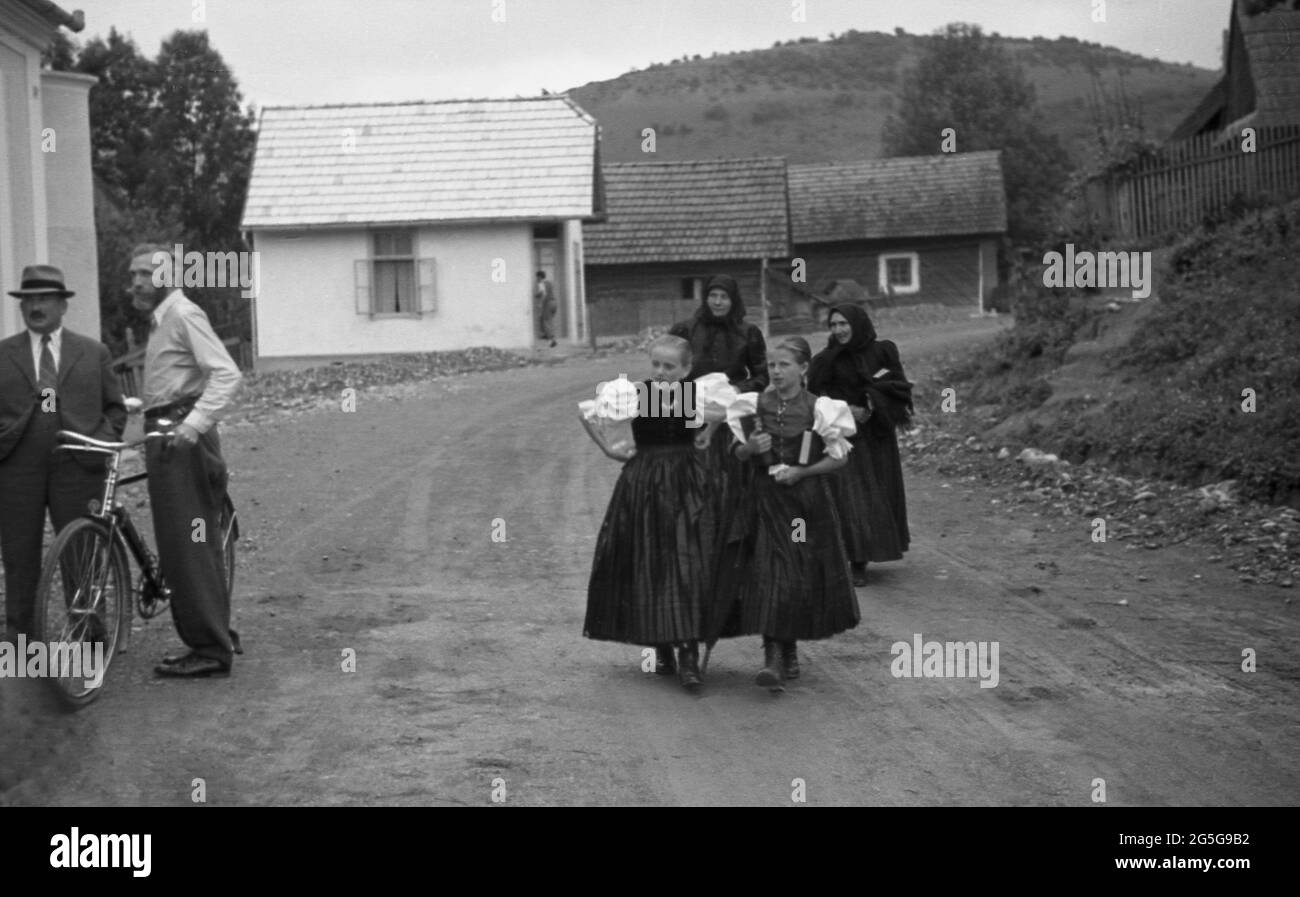 1930s, village rural historique en Bohême, gens, deux filles tchèques en jupes longues traditionnelles, deux femmes suivantes et deux hommes, une avec vélo, bavardant. Cette région de la Tchécoslovaquie était connue et surnommée à cette époque les Sudètes, nom historique du peuple allemand des sudètes vivant dans les pays de Bohême occidentale et d'autres régions frontalières. Banque D'Images