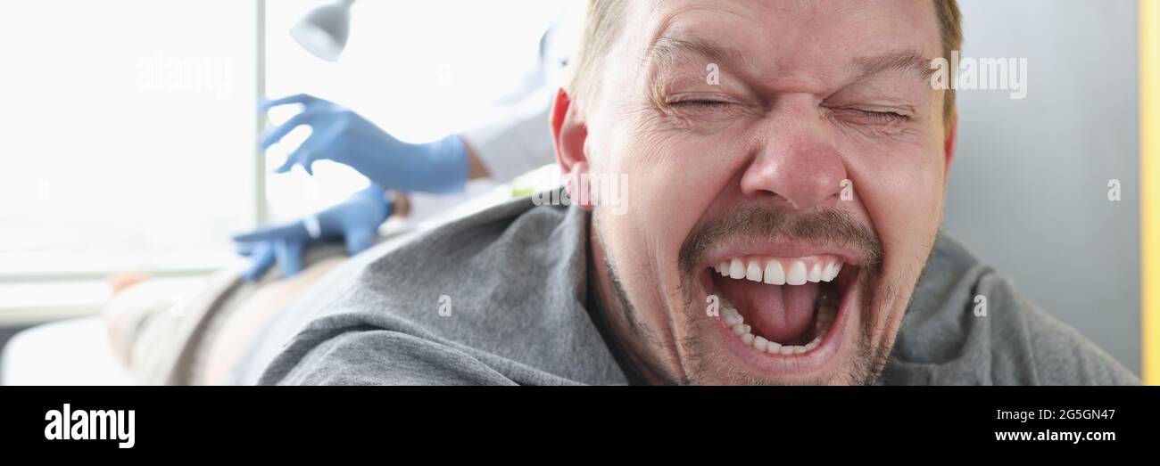 Homme allongé sur un canapé avec sa bouche ouverte. Infirmière donnant l'injection dans la fesse Banque D'Images