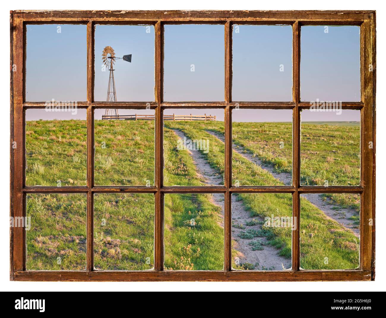 route de terre dans une prairie verte menant à un moulin à vent avec une pompe à eau dans une prairie courte vue d'une fenêtre à guillotine vintage Banque D'Images