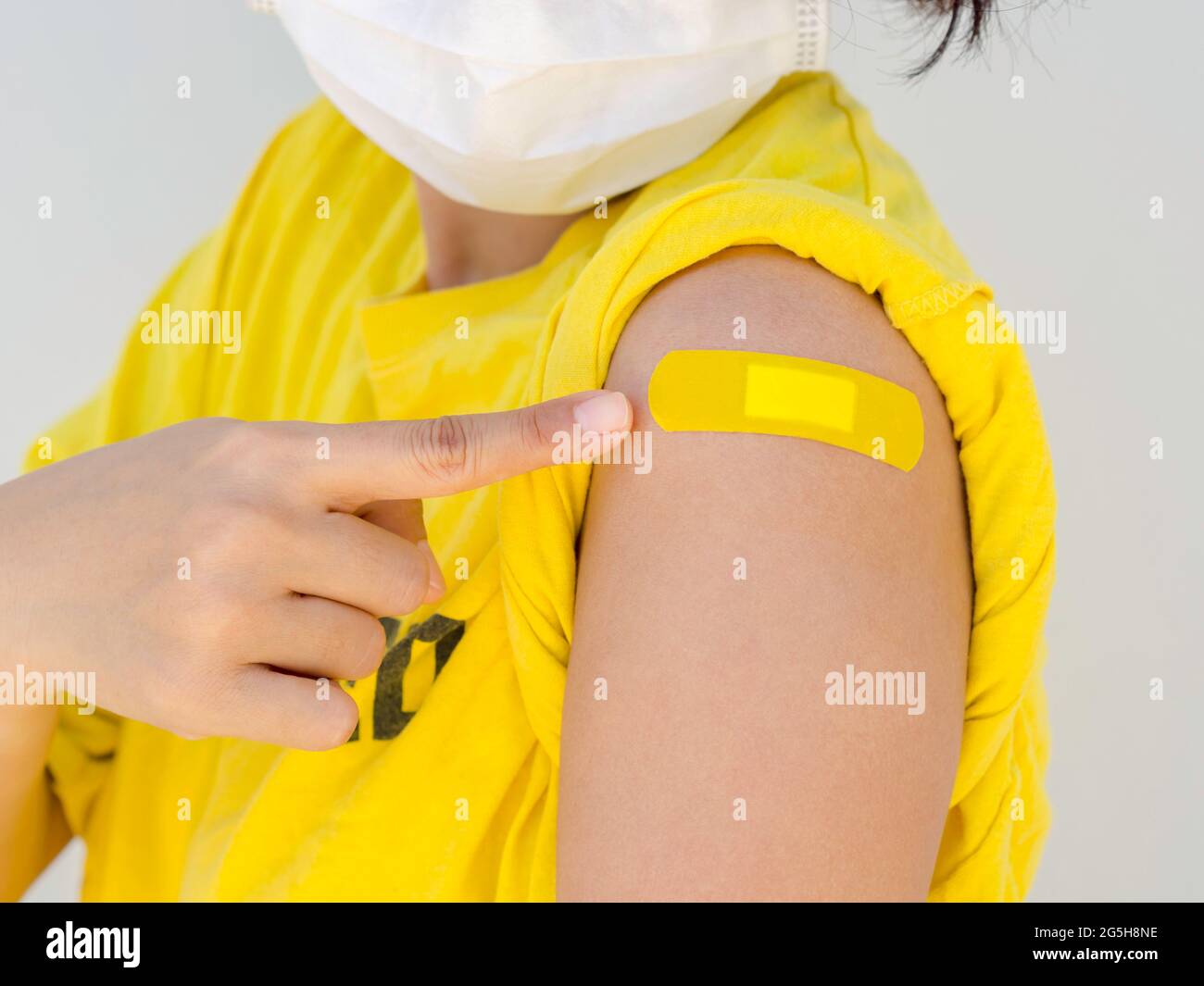 Vaccinations, pansement sur le concept de bras des femmes vaccinées. Main pointant sur le bandage adhésif jaune sur son épaule qui porte une chemise jaune, wh Banque D'Images