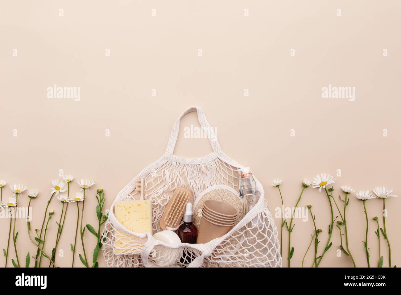 Concept d'été écologique sur fond beige avec sac d'achats écologique, fleurs de camomille blanches, accessoires de bain, brosses, bouteille d'huile essentielle, savon Banque D'Images