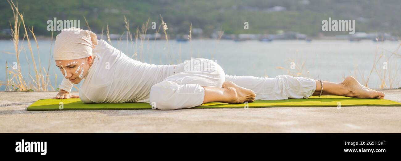 Kundalini yoga femme en vetements blancs et turban pratique le yoga kundalini sur le fond de la mer des montagnes et du coucher du soleil. Peinture de visage de combat Photo Stock
