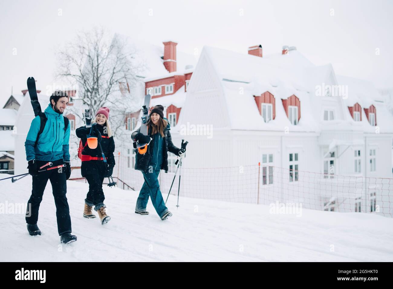 Pleine longueur d'amis féminins et masculins parlant les uns avec les autres tout en marchant sur la neige Banque D'Images