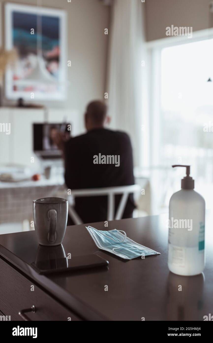 Désinfectant pour les mains et masque sur la table pendant que le professionnel masculin est en arrière-plan à la maison pendant une pandémie Banque D'Images