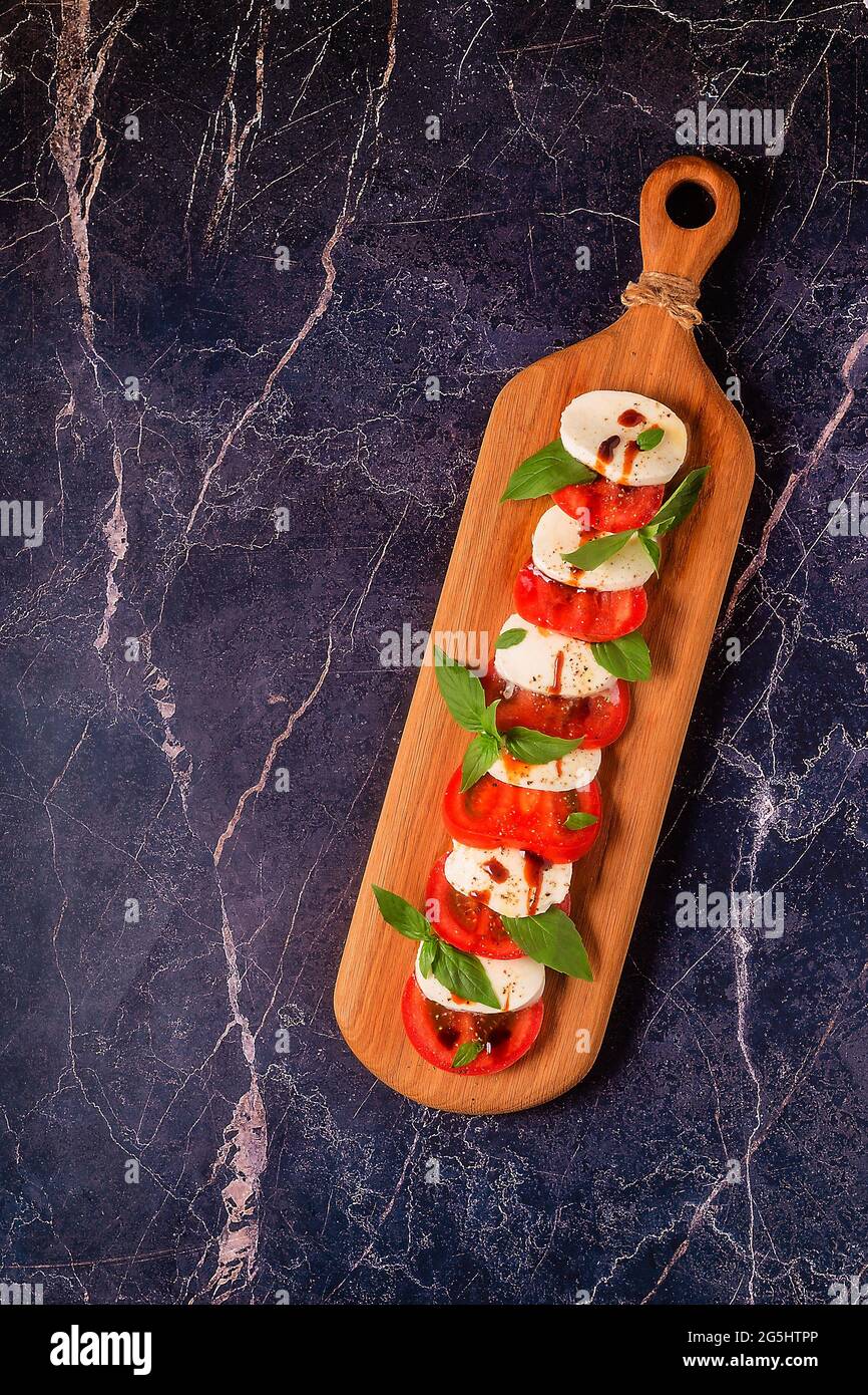 Salade de caprese italienne avec tomates en tranches, mozzarella, basilic, huile d'olive sur un plateau de service en bois. Banque D'Images