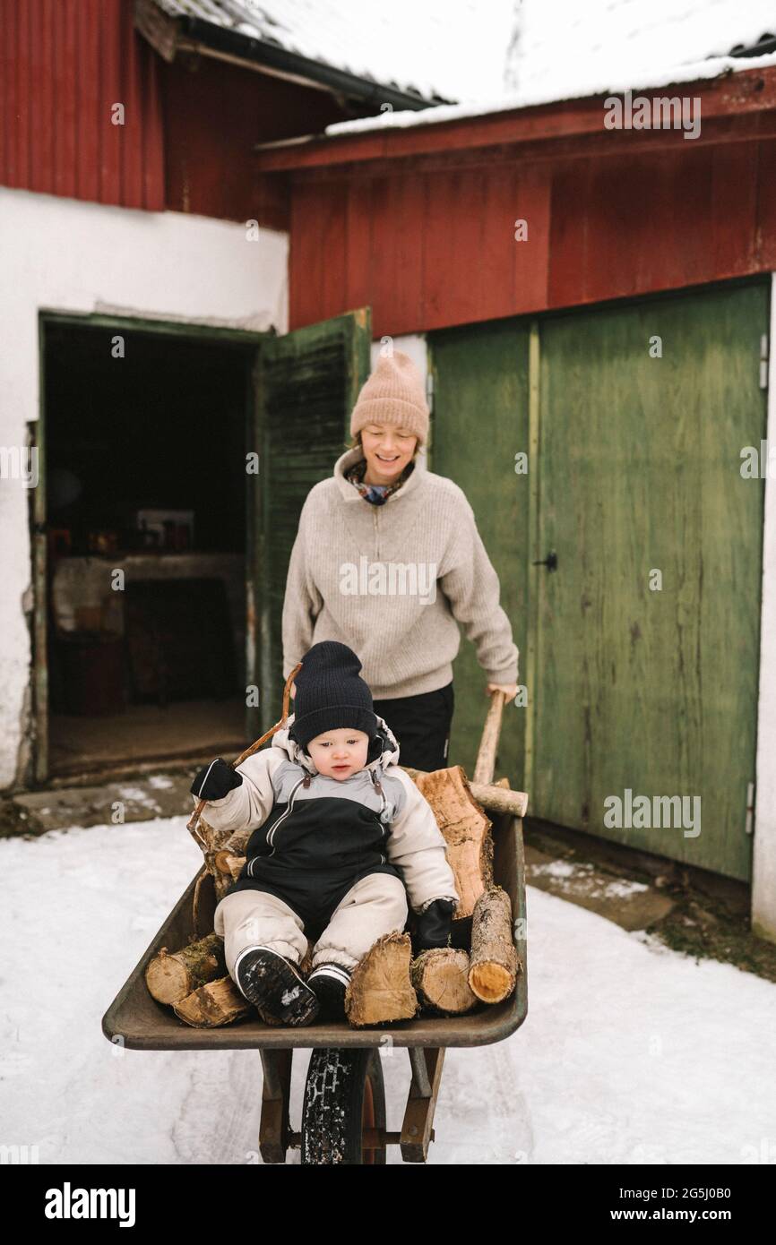 Une mère souriante portant sa fille assise sur du bois de chauffage dans une brouette pendant l'hiver Banque D'Images