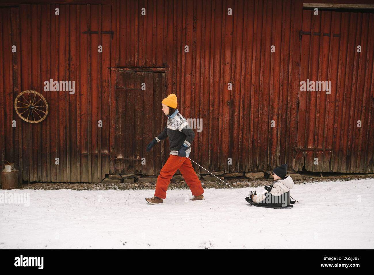 Femme mature tirant sa fille sur le toboggan en marchant dans le cottage pendant l'hiver Banque D'Images