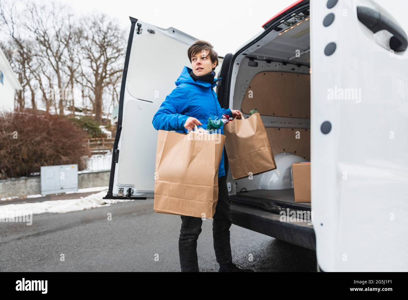 Une personne de livraison féminine déchargeant des sacs en papier de la camionnette Banque D'Images