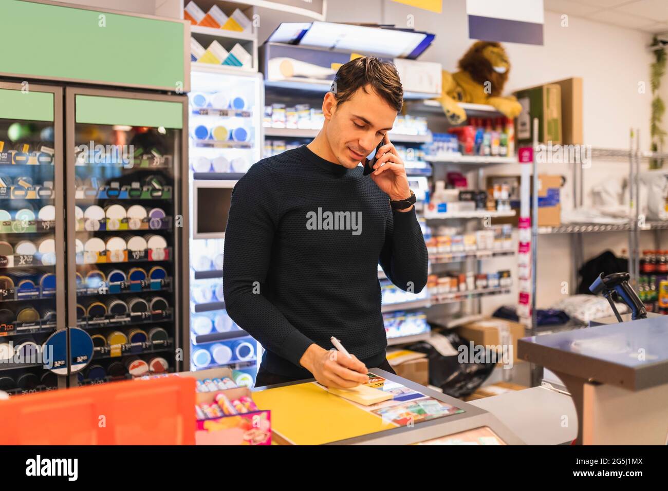 Un homme écrit par le propriétaire d'un magasin en parlant sur un téléphone portable au moment de la caisse Banque D'Images