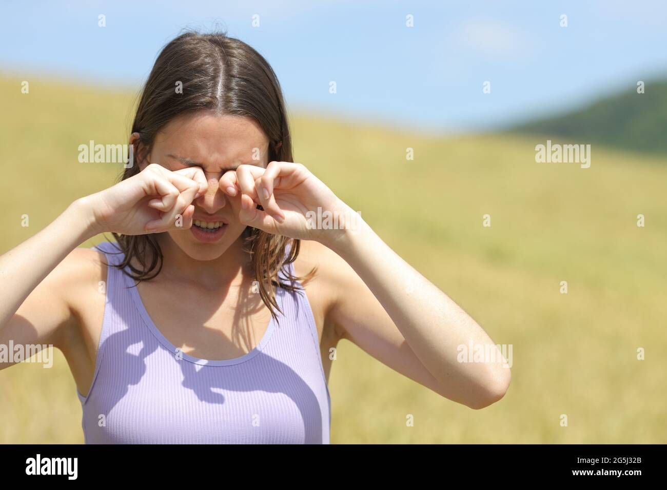 Vue de face d'une femme allergique qui se gratte les yeux dans un champ de blé Banque D'Images