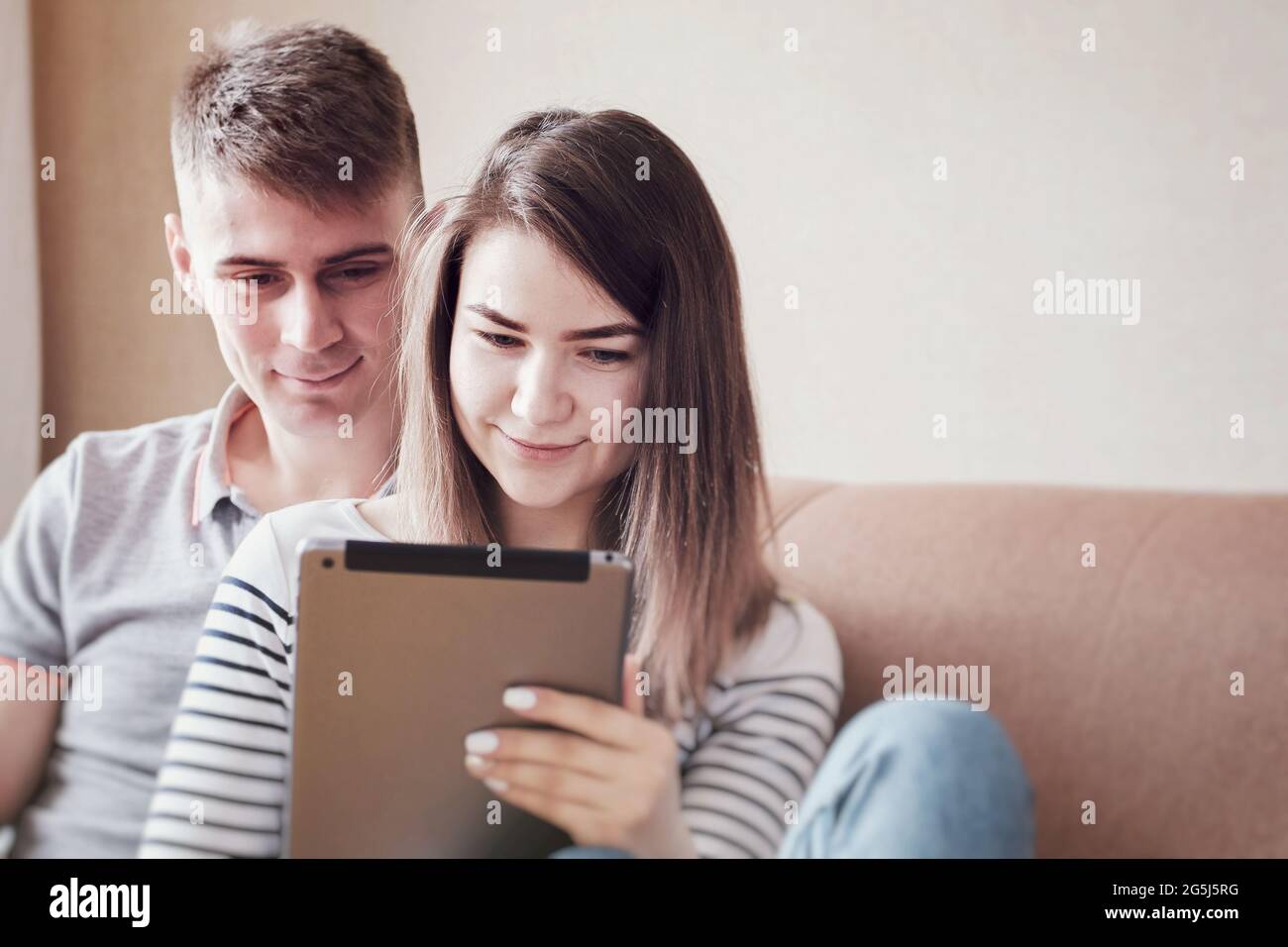Le jeune homme épouse doucement sa petite amie et sa femme et regarde le contenu sur la tablette - Jeune couple se détend sur le canapé et fait des achats en ligne Banque D'Images